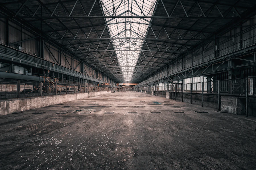 Vast empty steel-framed industrial hall with a long roof monitor and daylight falling across the floor