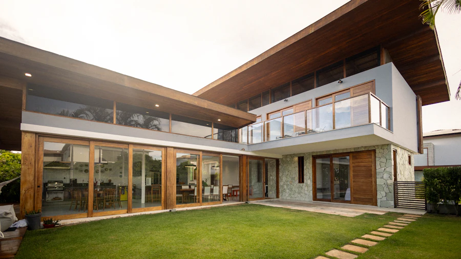 Two-storey modern house with timber soffits and floor-to-ceiling glass opening onto a lawn